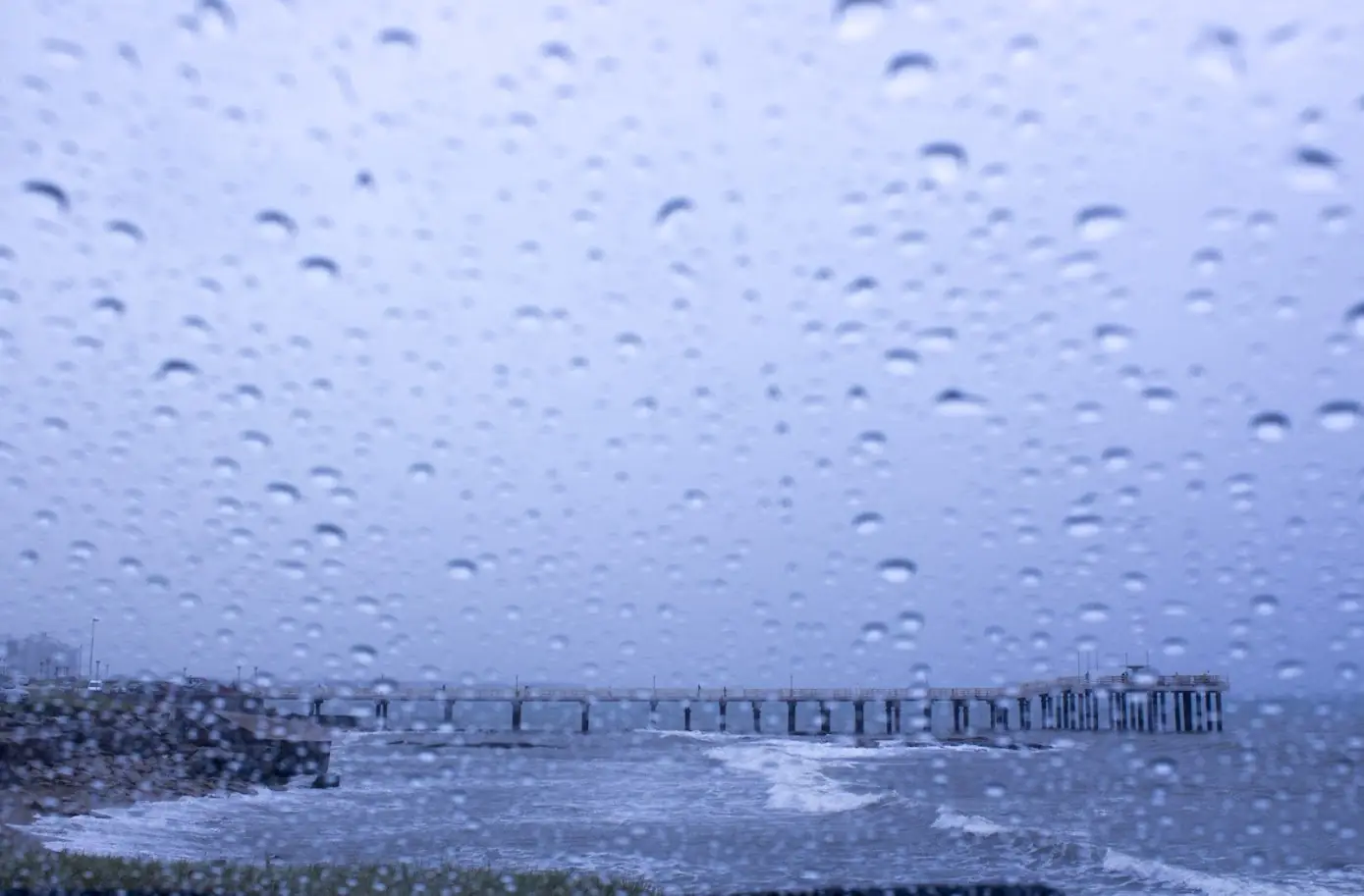 Muelle sobre el mar en un día de lluvia, visto a través de un vidrio con gotas